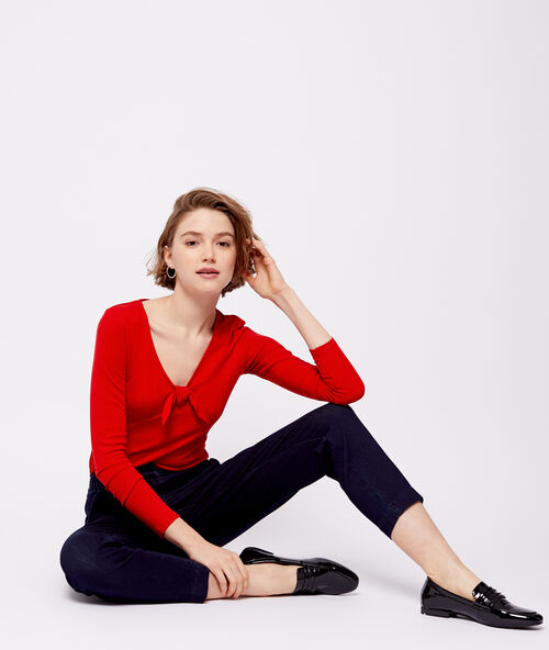Camiseta escotada con lazo descorativo rojo.
